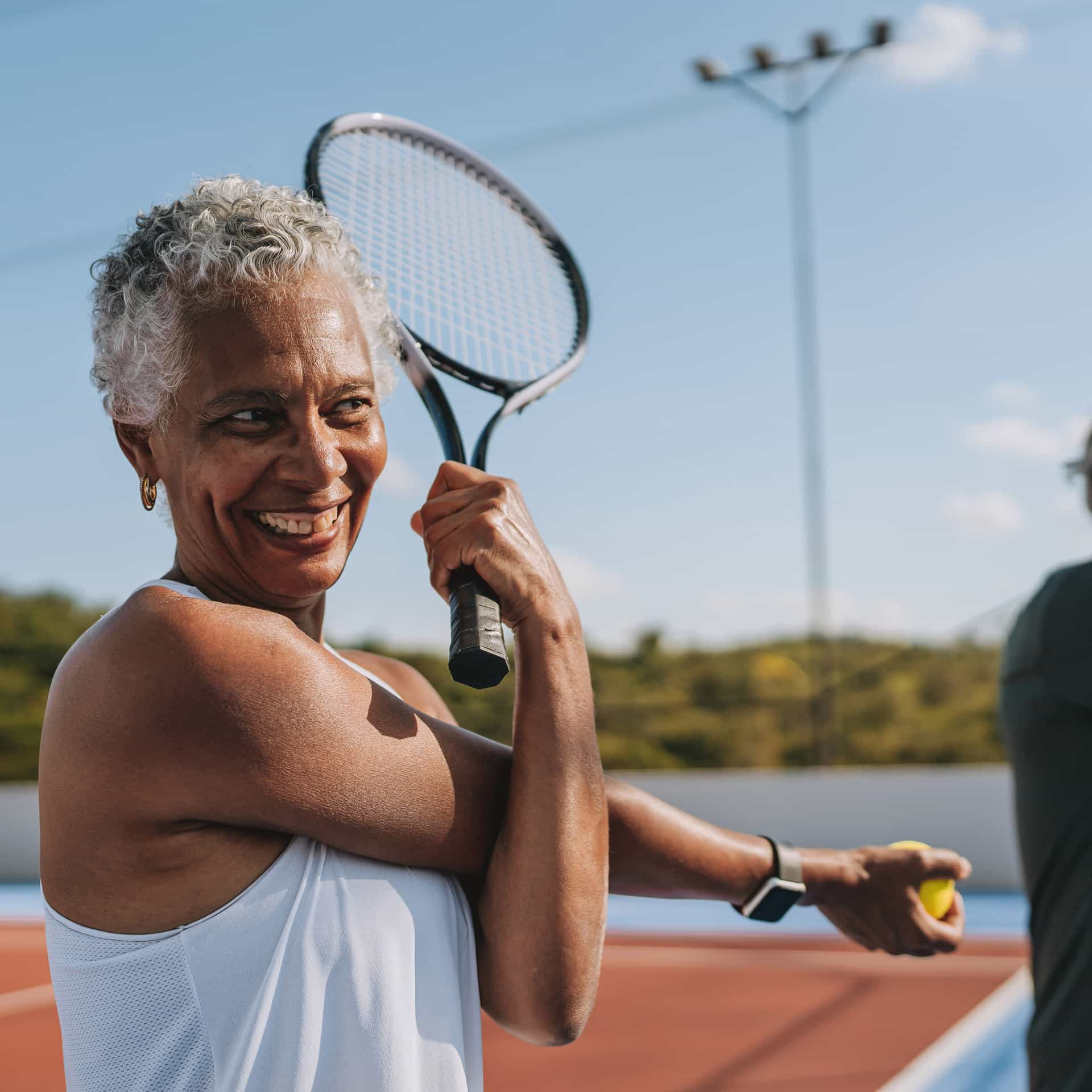 A senior woman stretches before playing tennis outdoors on a sunny day